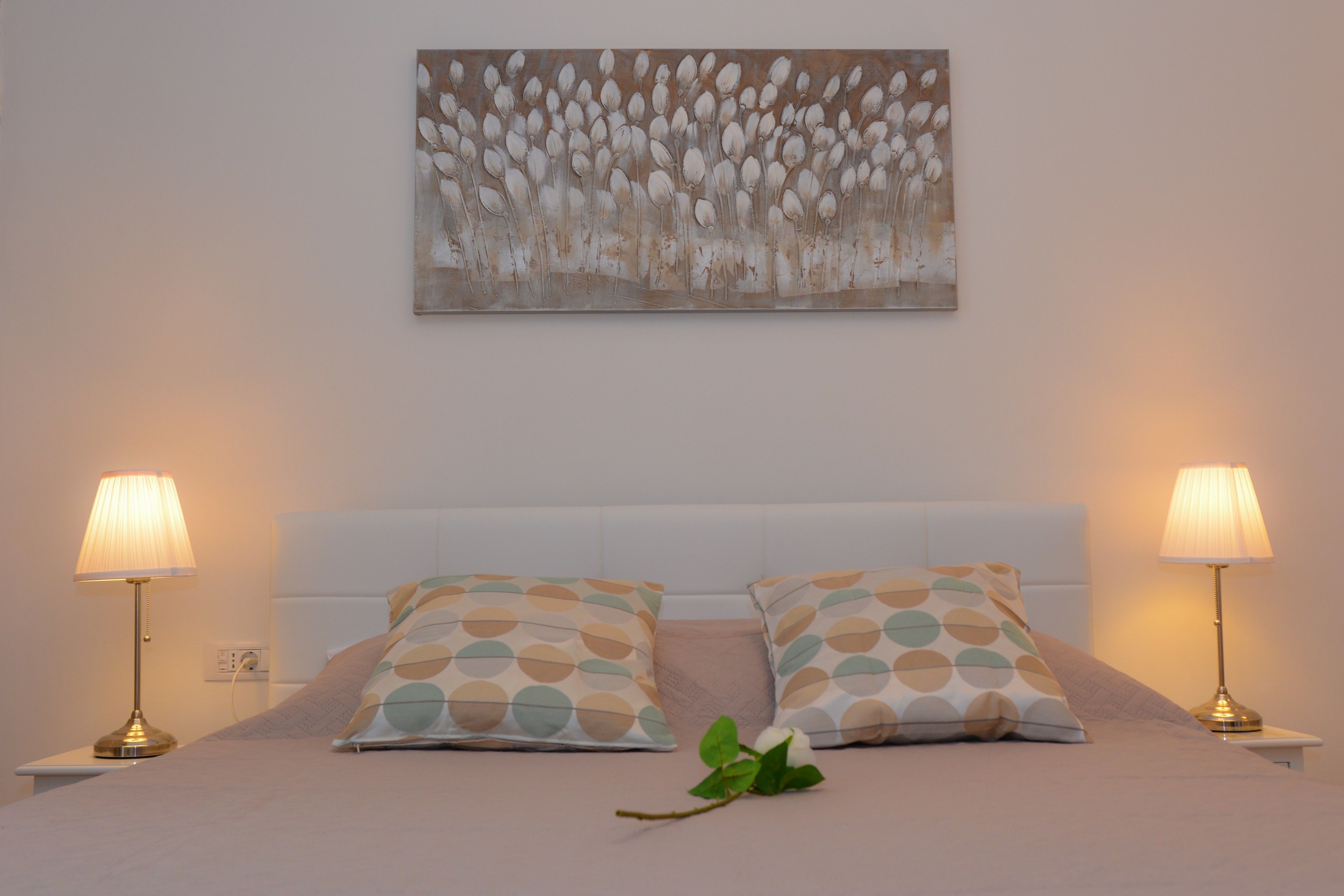 A neatly made bed with patterned pillows, a wall-mounted abstract painting, and two bedside lamps.