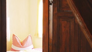 A bedroom with a wooden door, a bed with striped pillows, and a window with curtains.