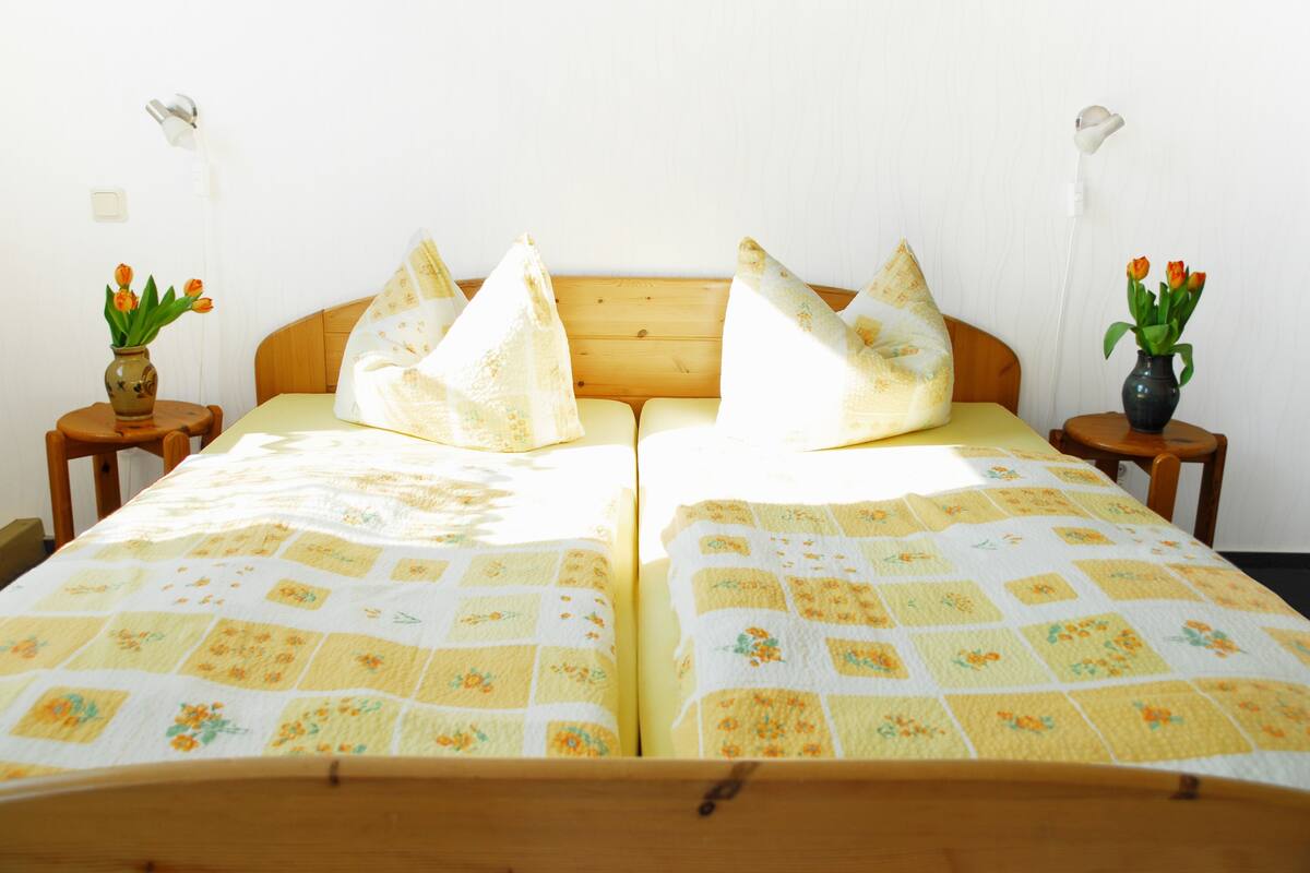 A double bed with a floral quilt, two bedside tables with vases of flowers, and a wooden headboard.