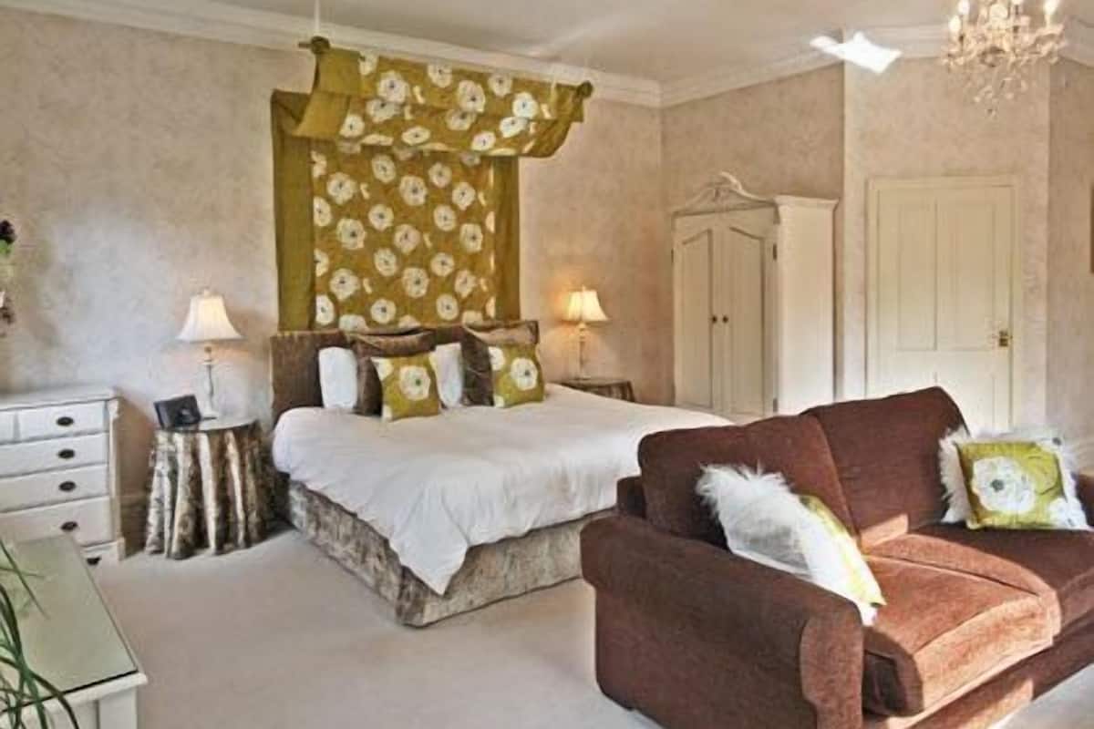 A bedroom with a bed, a brown sofa, a wardrobe, and a chandelier.