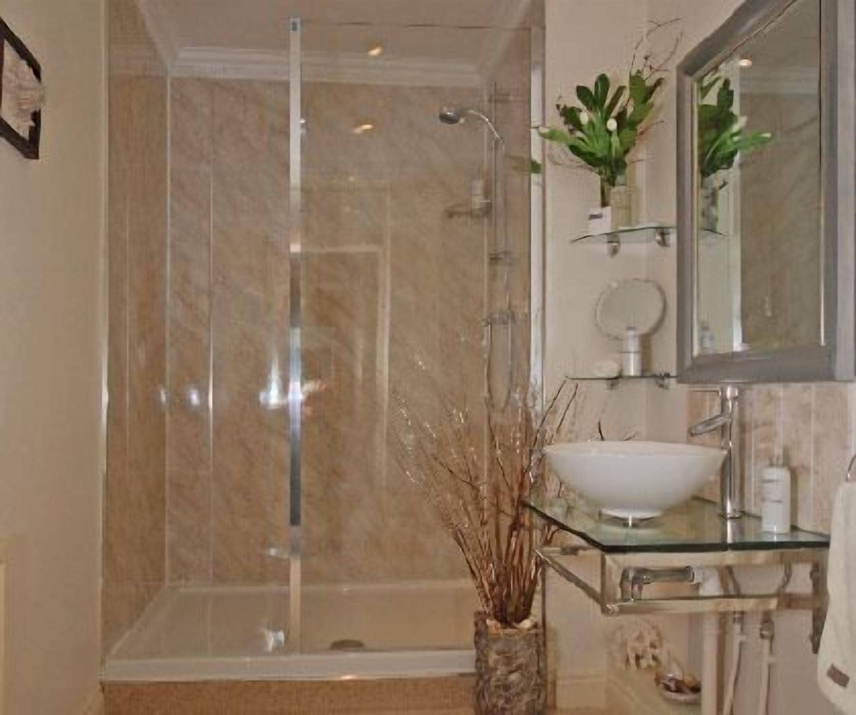 A bathroom with a glass-enclosed shower, a glass sink, and a mirror above the sink.