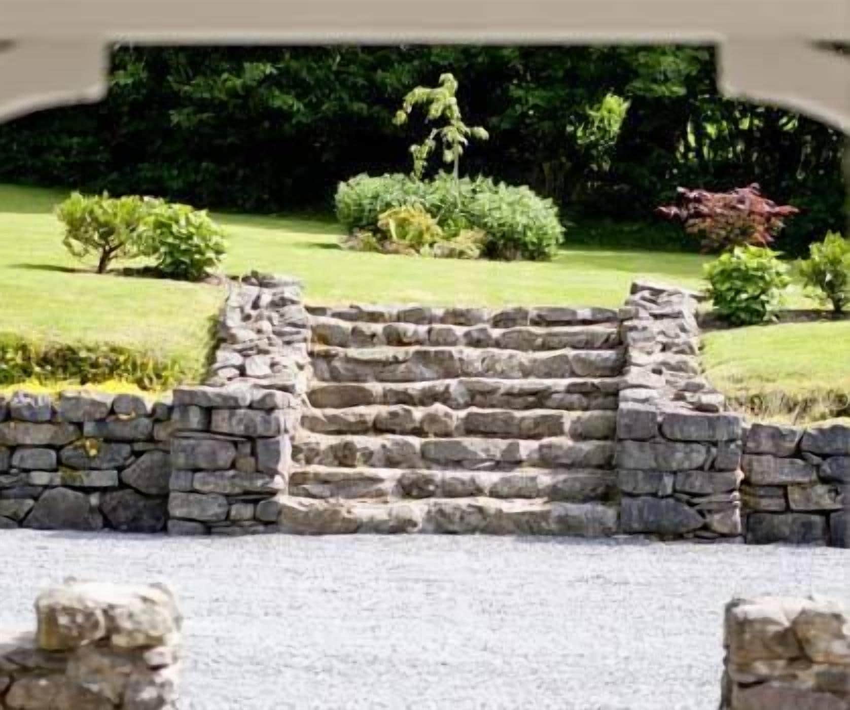 A stone staircase leading up to a building entrance, surrounded by a well-maintained lawn and various shrubs.