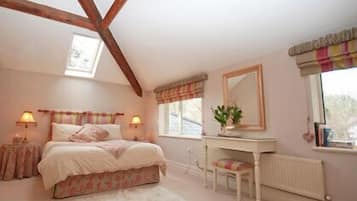 A bedroom with a bed, bedside tables, a desk, a chair, a radiator, and a window with curtains.