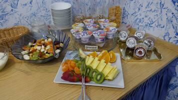 Una mesa de buffet con diversas opciones de comida, incluyendo frutas, Granini y vasos de yogur.