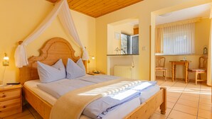 A bedroom with a wooden bed, a nightstand, a bedside table, a window with curtains, and a small table with chairs. - Villa Tummelchen (Cochem)