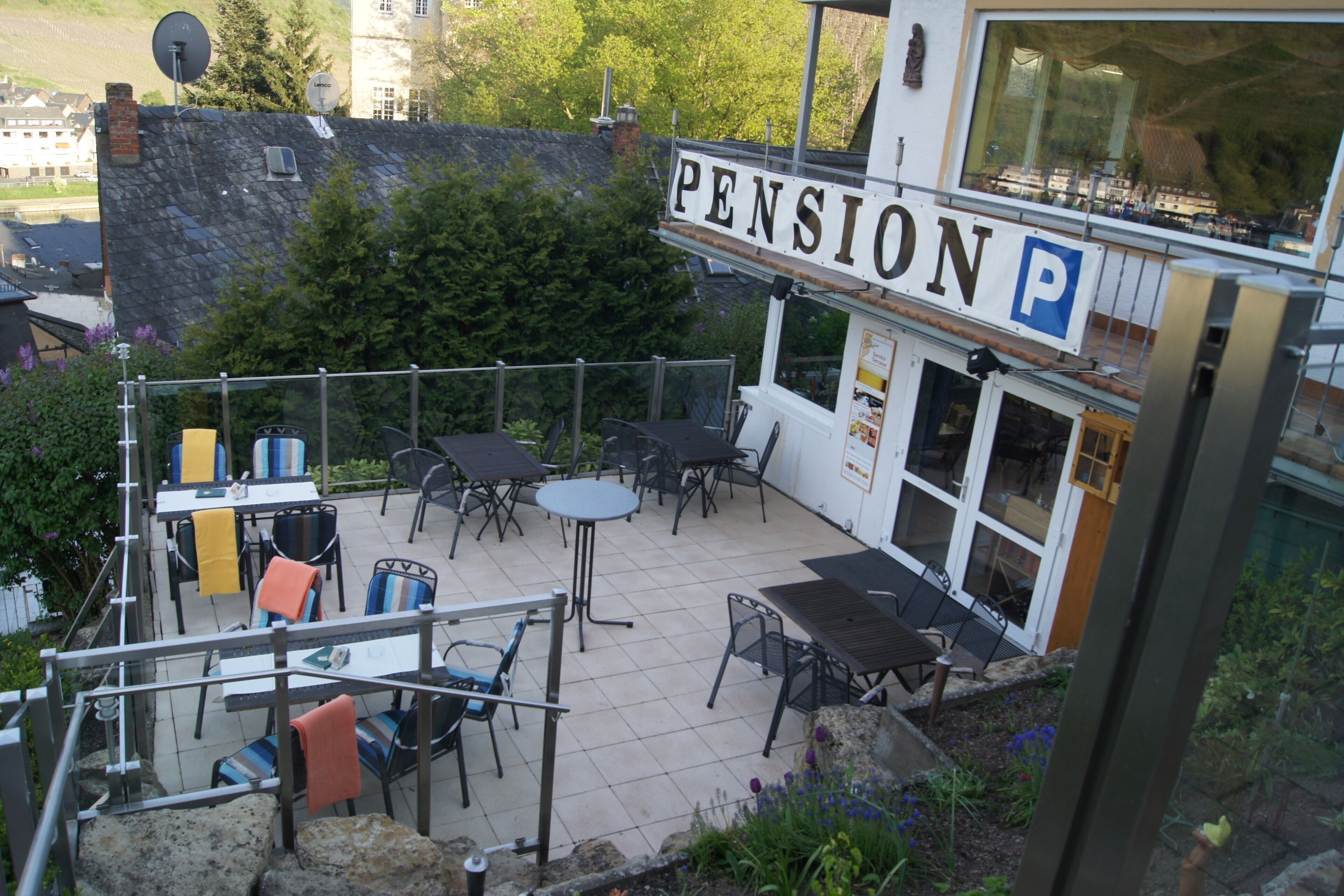 Un patio al aire libre con mesas y sillas, un cartel que dice "PENSION" y vistas de los alrededores.