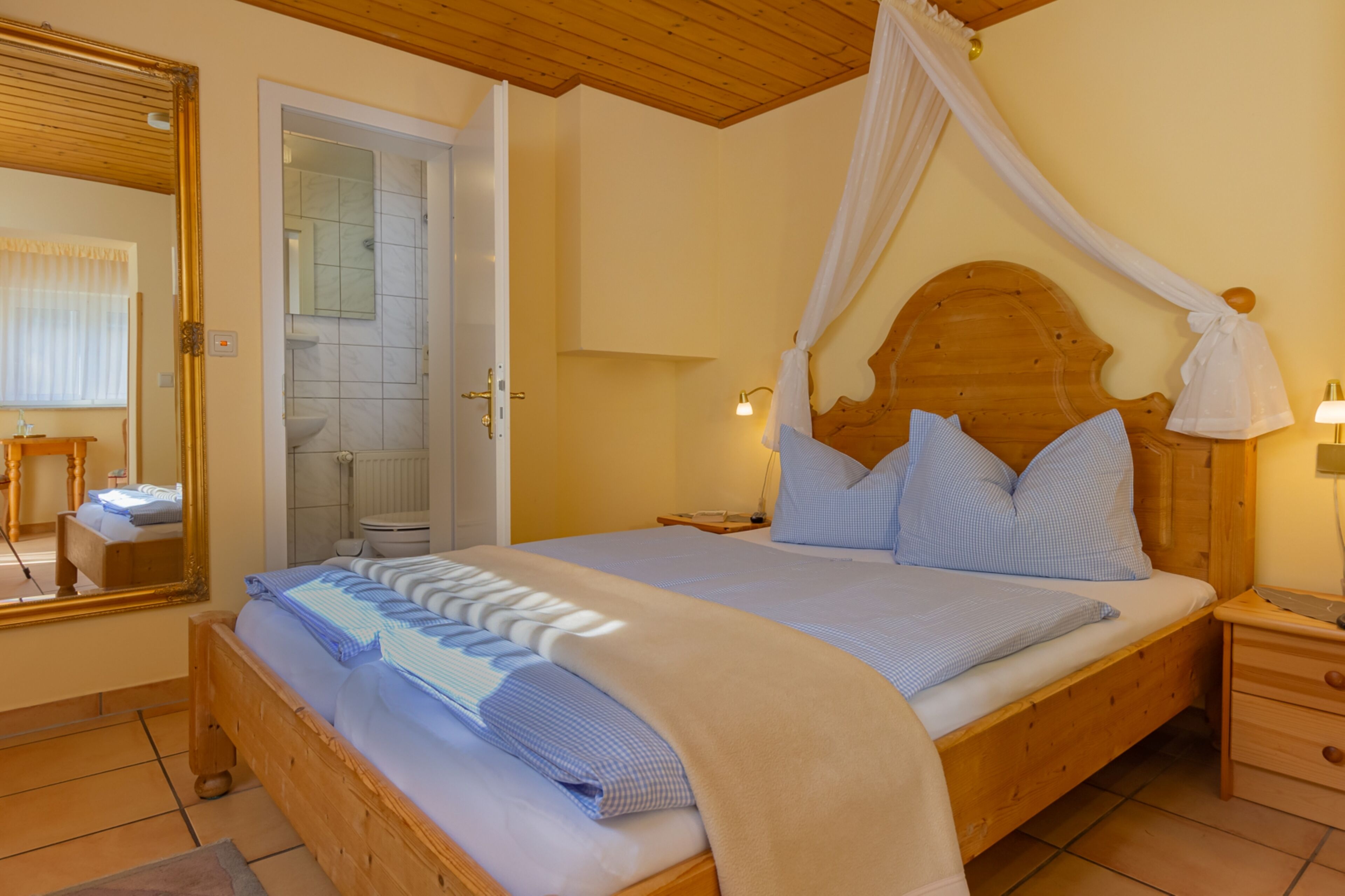A bedroom with a wooden bed, a canopy, a bedside table, and a nightstand.