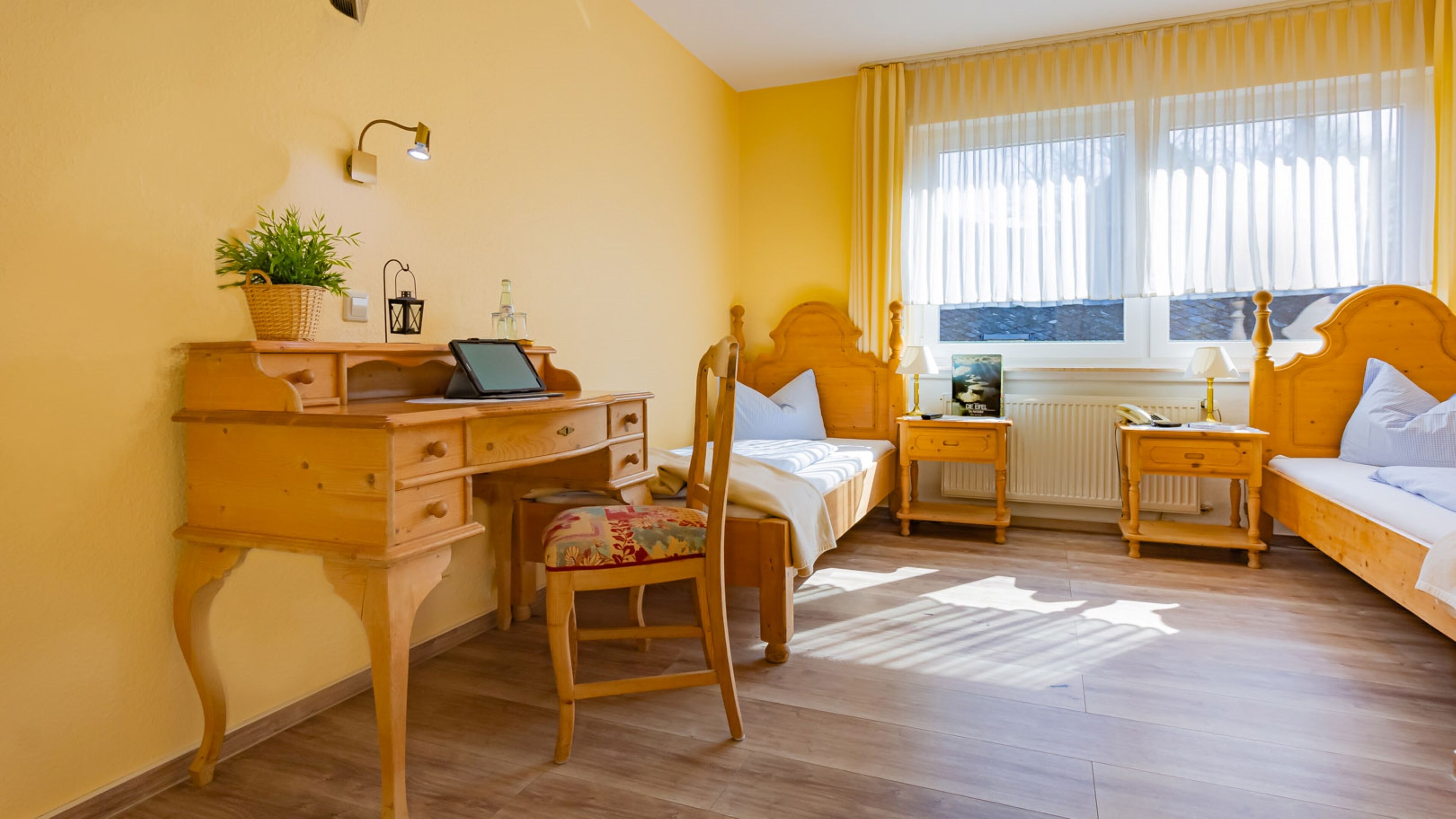 A room with a wooden desk, a bed, a chair, and a window with curtains.