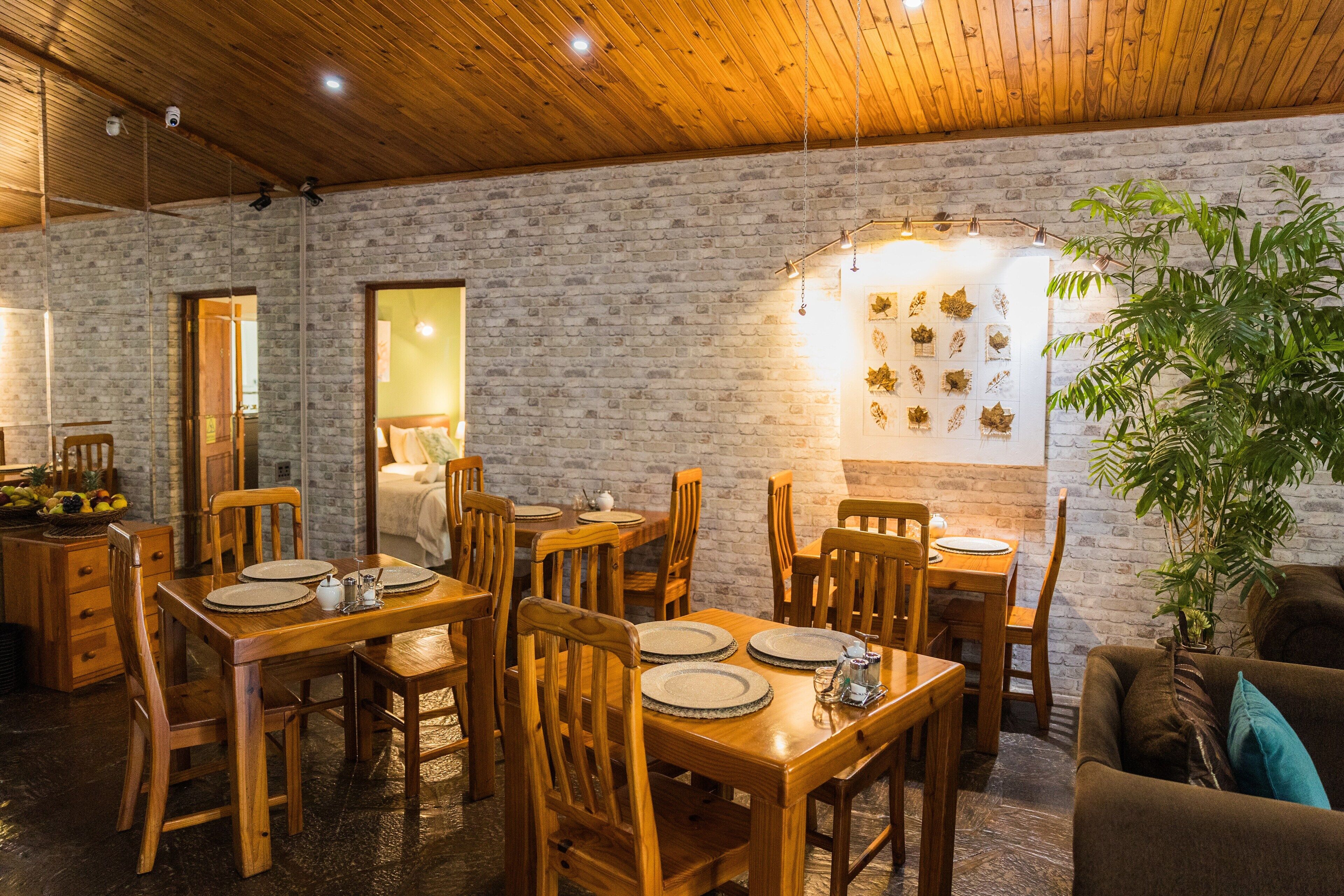Un comedor con mesas y sillas de madera, una pared de ladrillo y una planta en maceta.