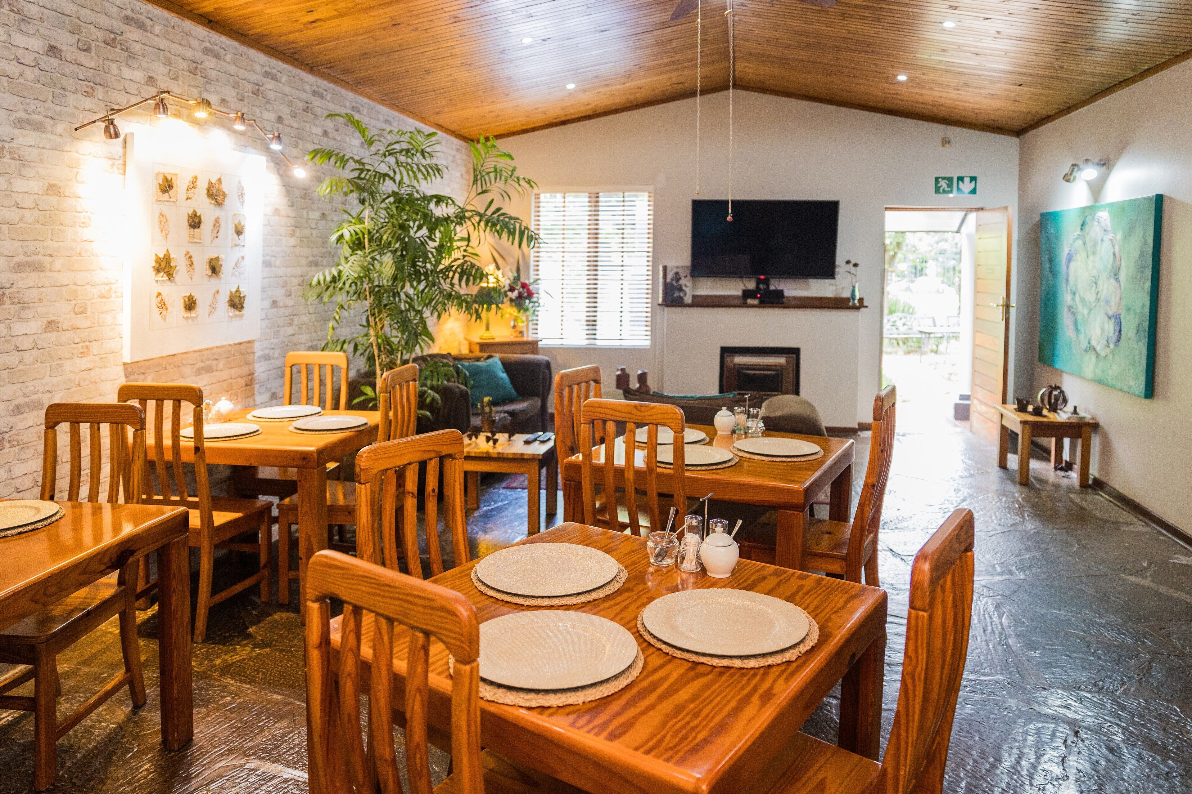 Un comedor con mesas y sillas de madera, una pared de ladrillo y un televisor montado.