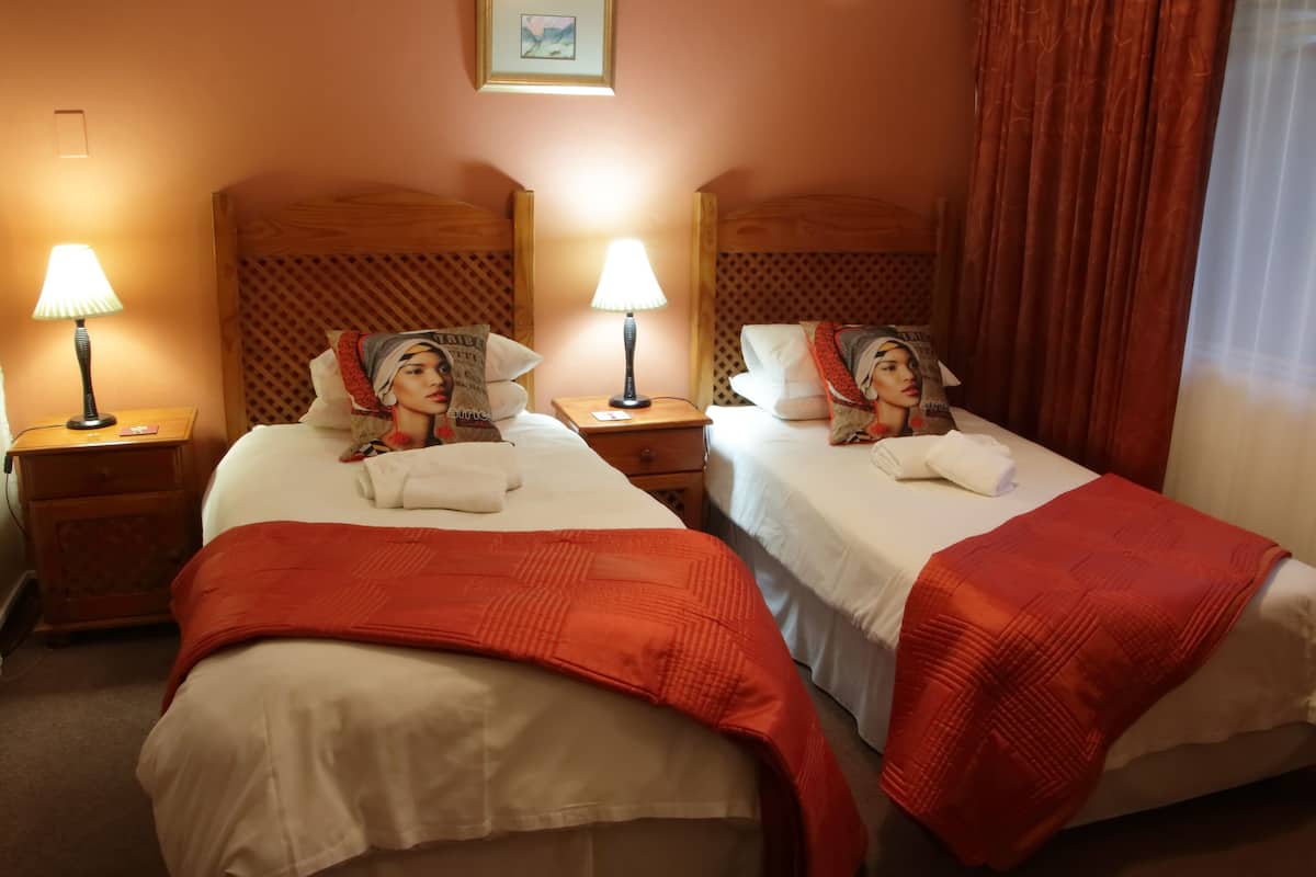 A hotel room with two beds, each with a red blanket, a wooden headboard, and a nightstand with a lamp.