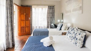 Habitación de hotel con dos camas, un ventilador de techo, una ventana con cortinas y un cuadro en la pared.