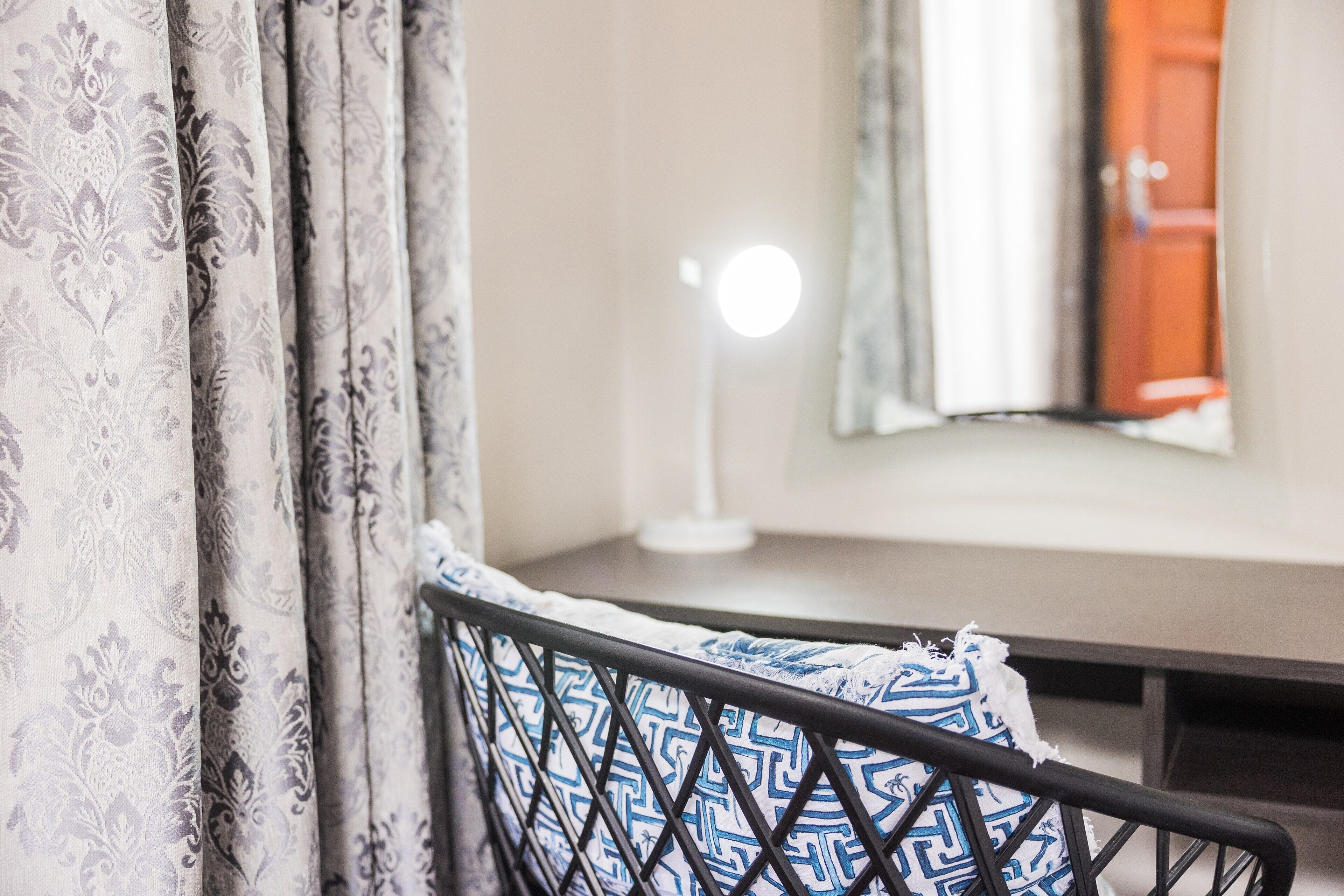 A bed with a patterned pillow, a bedside table with a lamp, and curtains with a floral pattern.