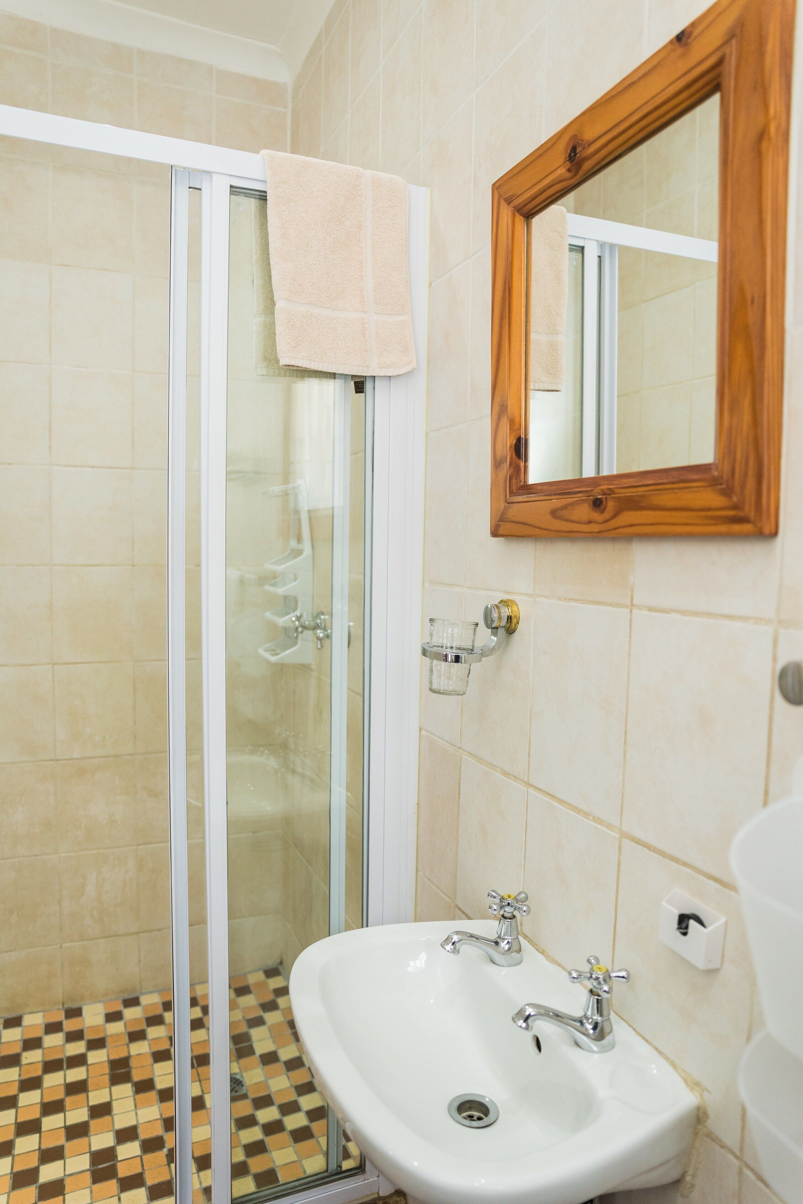 Un baño con cabina de ducha de vidrio, un lavabo doble y un espejo con marco de madera.