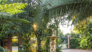 Un jardín con una fuente de piedra, un camino empedrado y abundante vegetación.