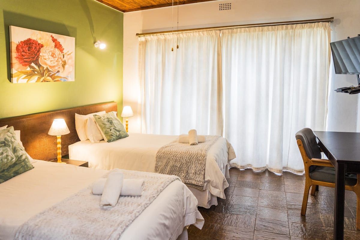 A hotel room with two beds, a desk, and a large window with curtains.
