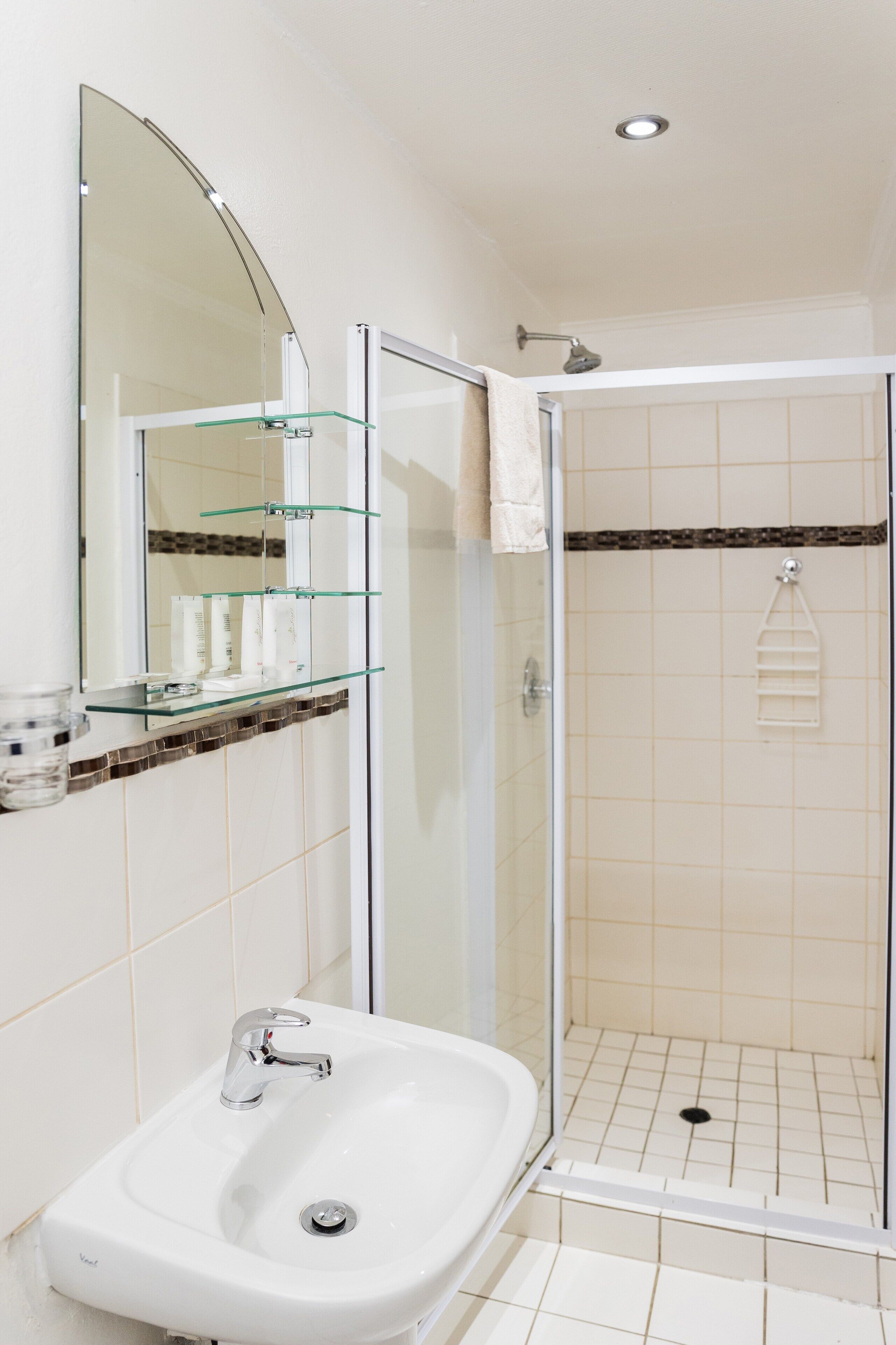Een badkamer met een douchecabine van glas, een wastafel met spiegel erboven en een glazen plank met toiletartikelen.