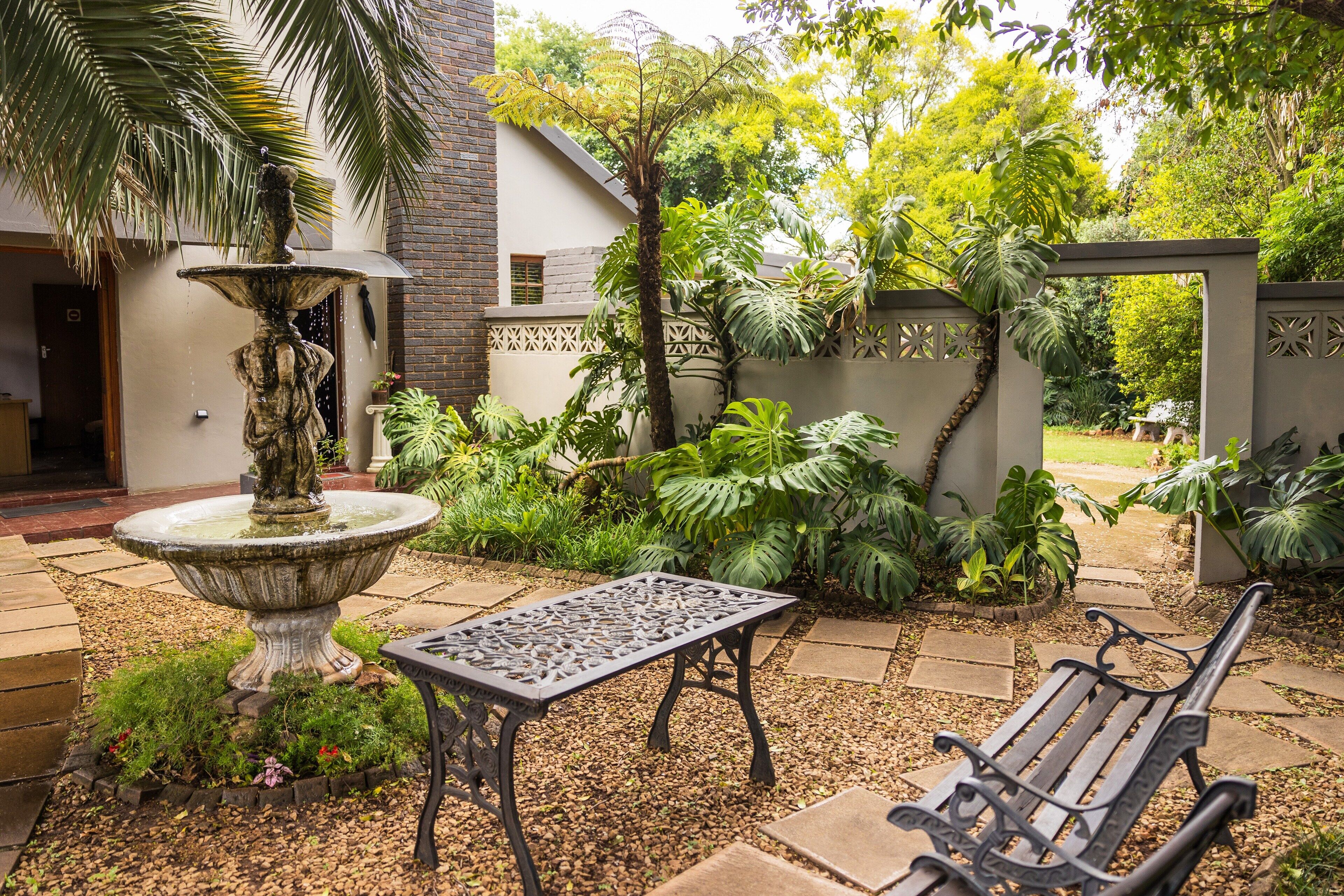 Um jardim com uma fonte de pedra, uma mesa de metal e um banco.