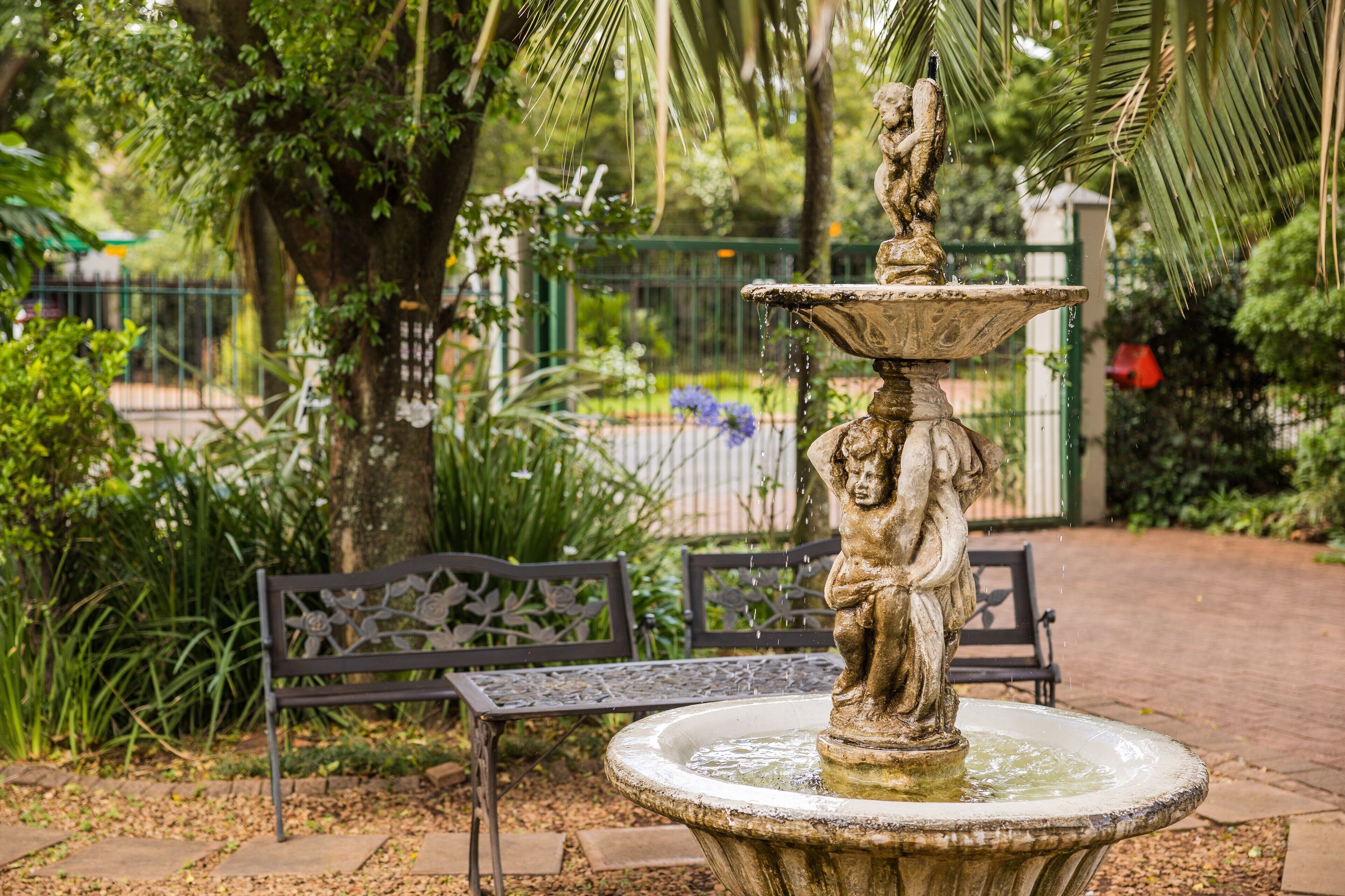 Uma fonte de pedra com estátua, rodeada por vegetação e um banco.