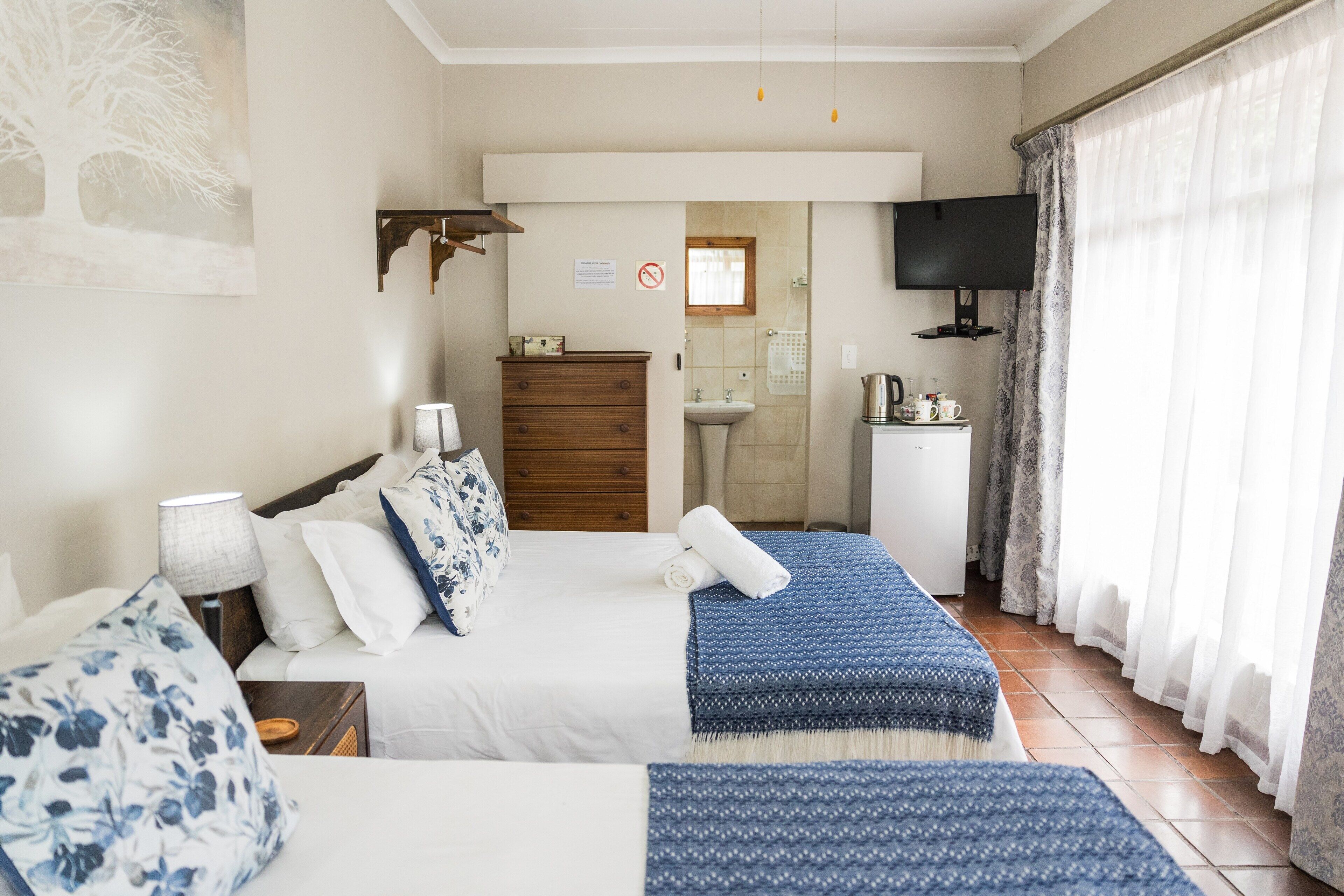 Un dormitorio con cama, mesitas de noche, cómoda, televisor y baño visible a través de una puerta abierta.