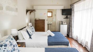Un dormitorio con cama, mesitas de noche, cómoda, televisor y baño visible a través de una puerta abierta.