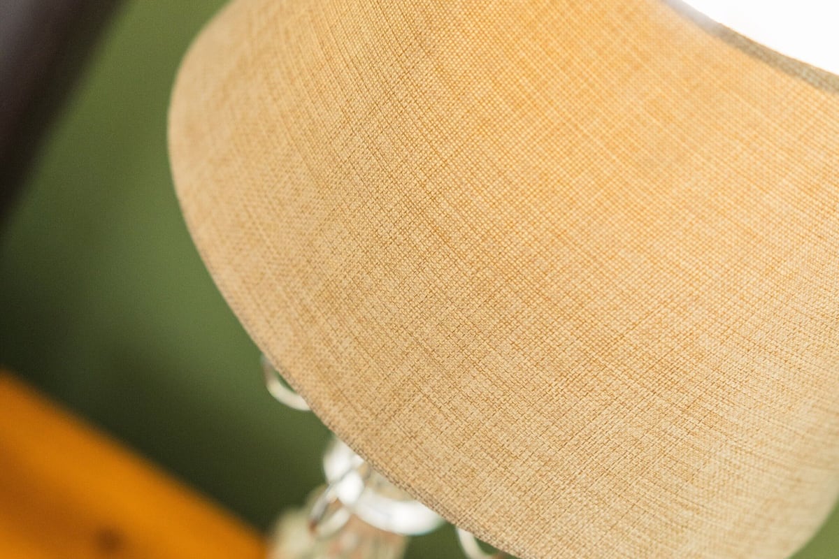 A close-up of a lamp with a beige fabric shade and a metallic base.