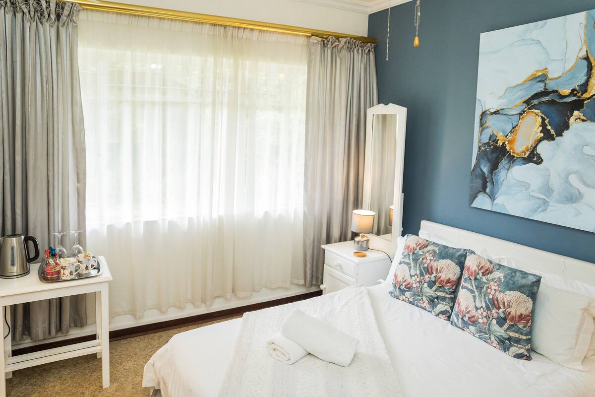 A neatly arranged bedroom with a bed, bedside table, and a large window with curtains.