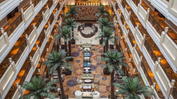 Un gran vestíbulo de hotel con un área de estar central, varios pisos y un mural decorativo en el techo.