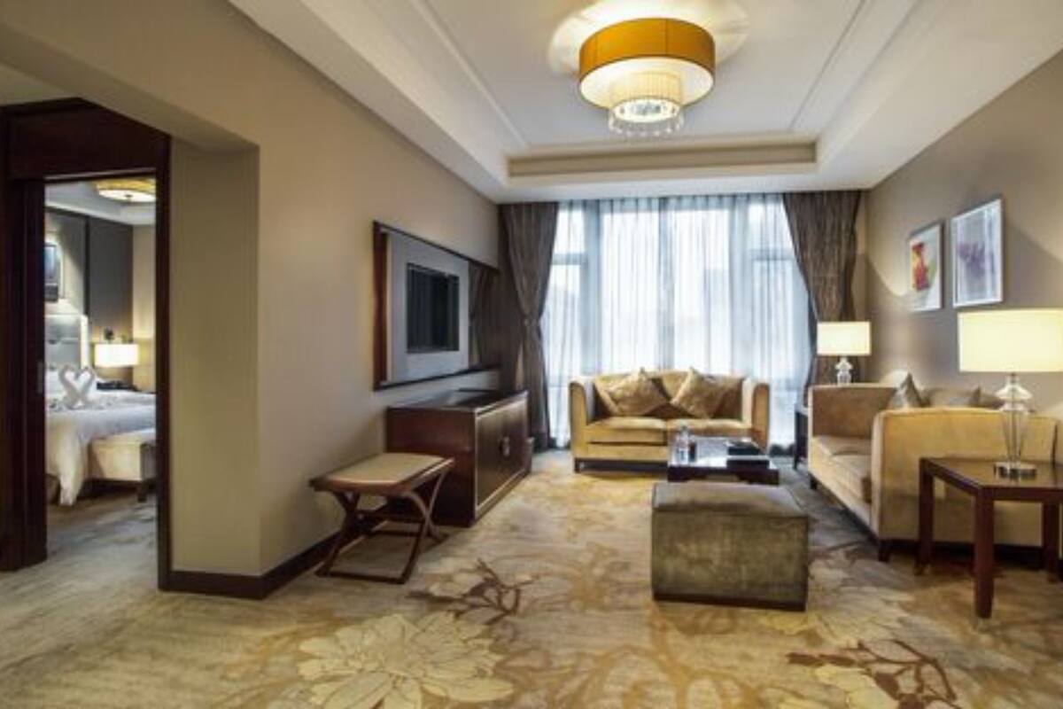 A hotel room with a large bed, a sitting area with a sofa and armchairs, a television, and a large window with curtains.