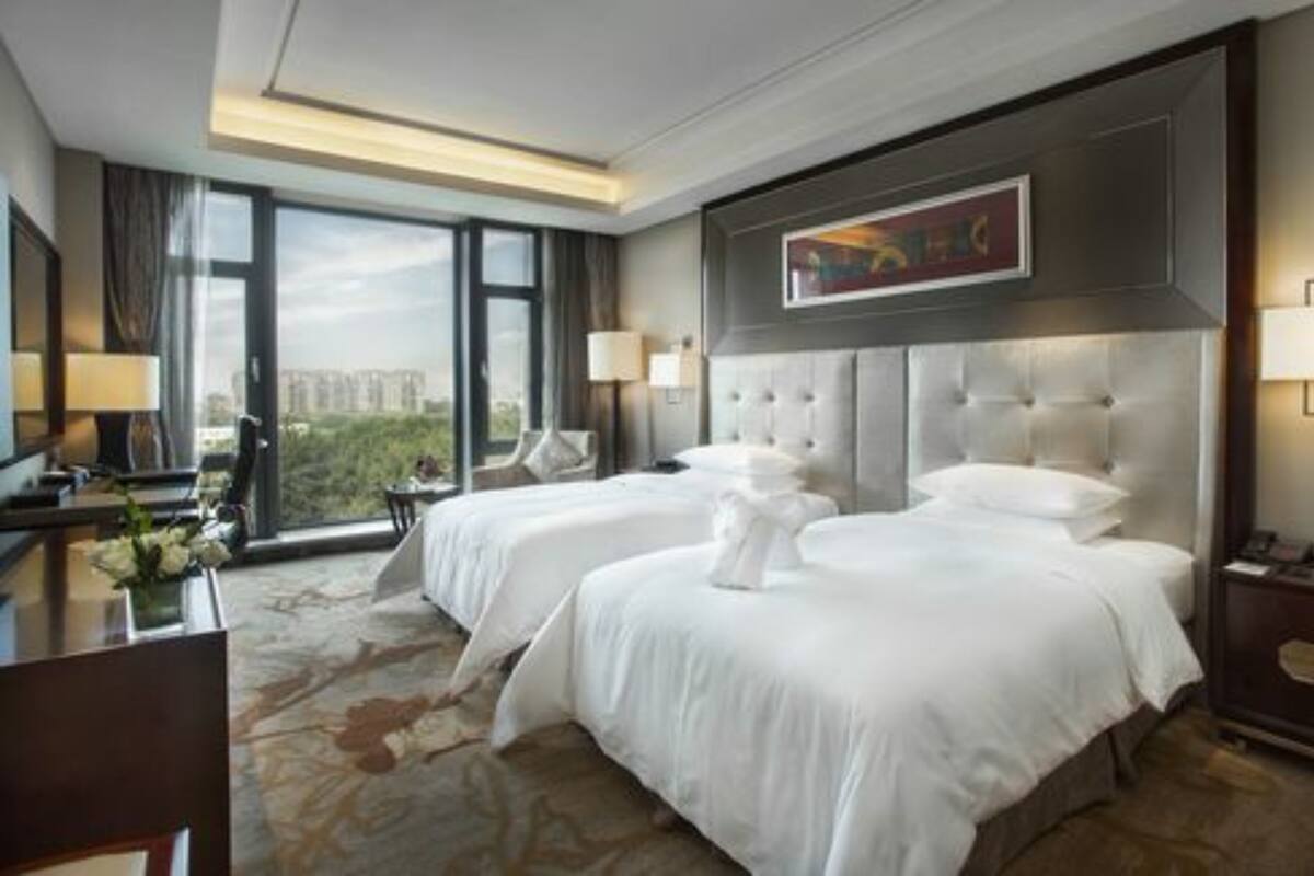 A hotel room with two beds, a desk, and a large window offering a city view.