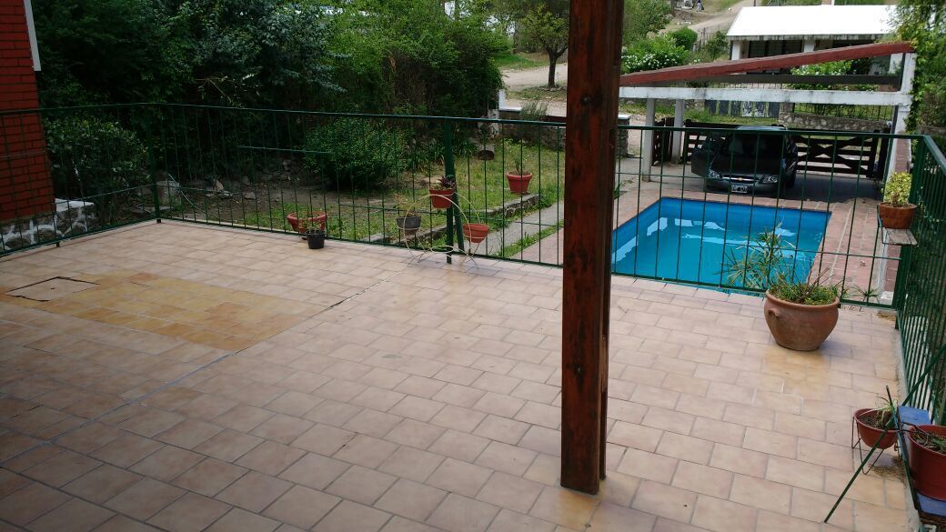 Un patio con piscina, rodeado por una valla verde y plantas en macetas.