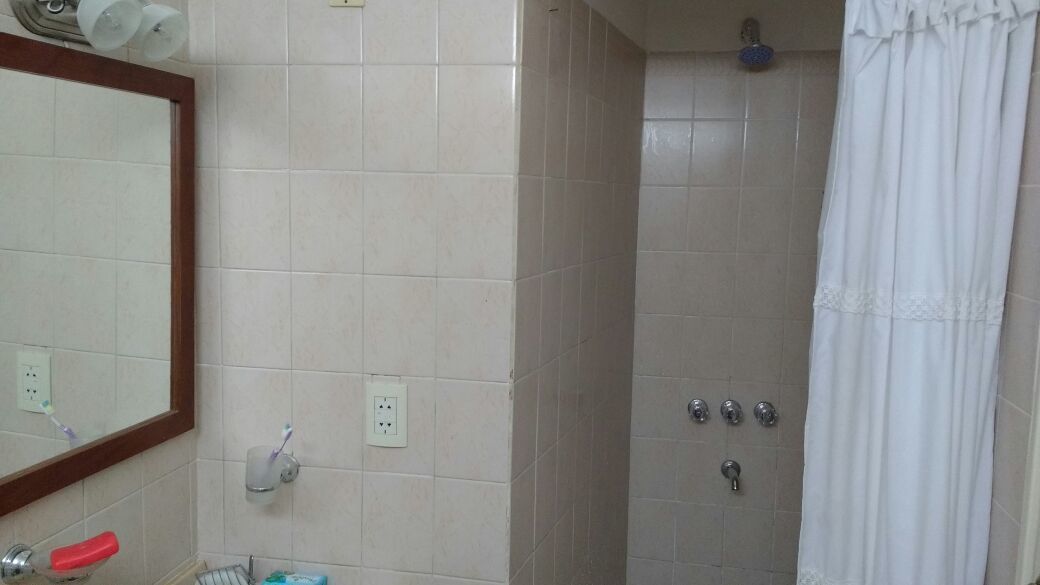 Un baño con espejo, lavamanos, ducha con cortina y retrete.