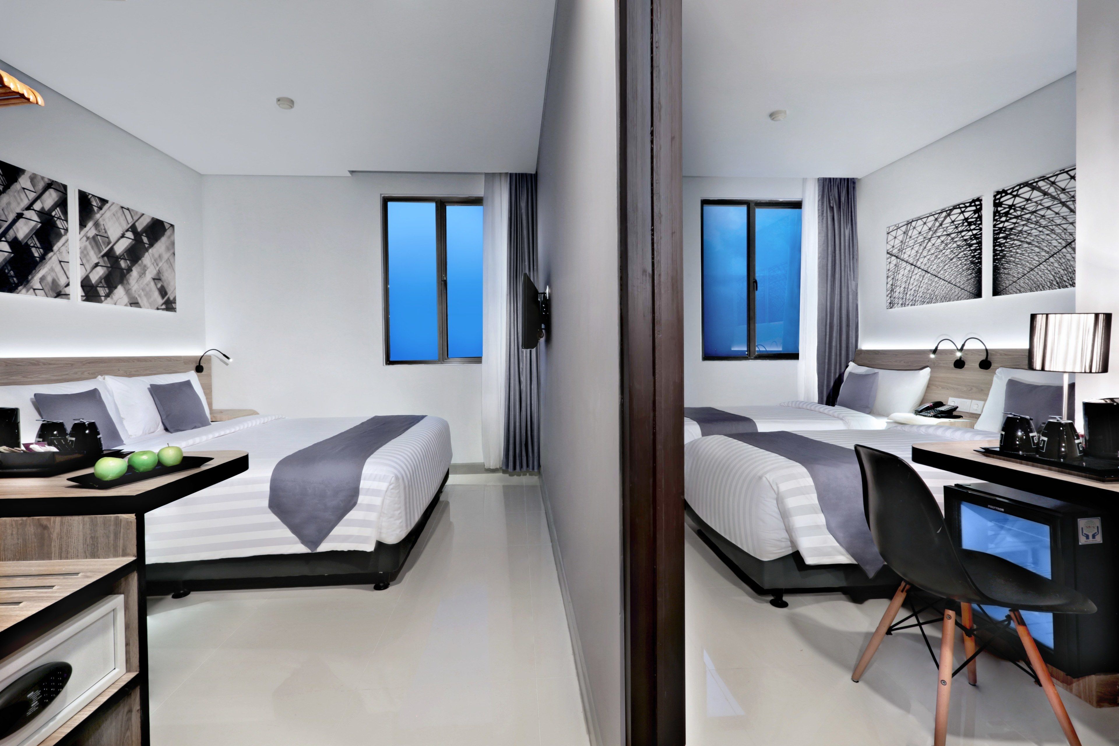 A modern hotel room with two beds, a desk, a chair, and artwork on the walls.