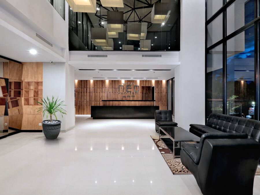Een moderne hotellobby met een receptiebalie, een zithoek en grote ramen met uitzicht over de stad.