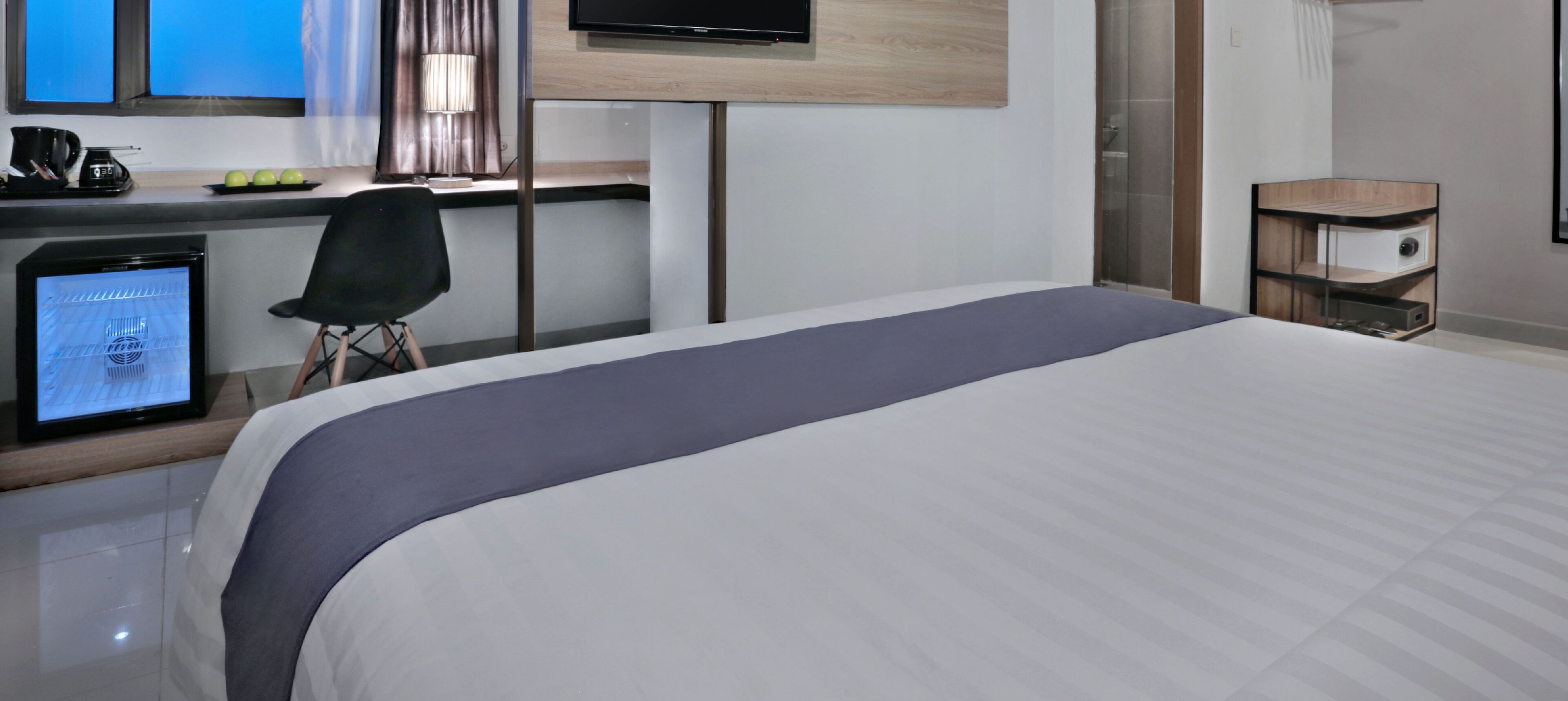 Habitación de hotel con cama, escritorio con computadora, silla y televisor montado en la pared.