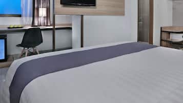 Habitación de hotel con cama, escritorio con computadora, silla y televisor montado en la pared.