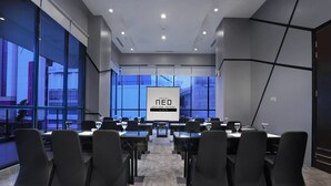 Moderni kokoushuone, jossa on suuri näyttö, jossa näkyy teksti ”HOTEL NEO”, ja suurista ikkunoista avautuu näkymä kaupungin ylle.