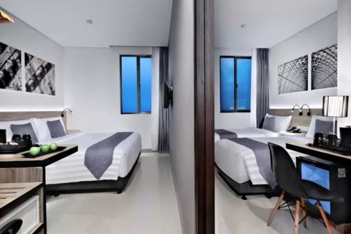 Moderni hotellihuone, jossa on kaksi sänkyä, työpöytä tietokoneella ja taideteoksia seinillä.