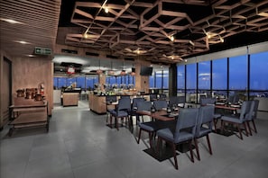 Ein modernes Restaurant mit hohen Decken und großen Fenstern, das einen Blick auf die Stadt bietet.