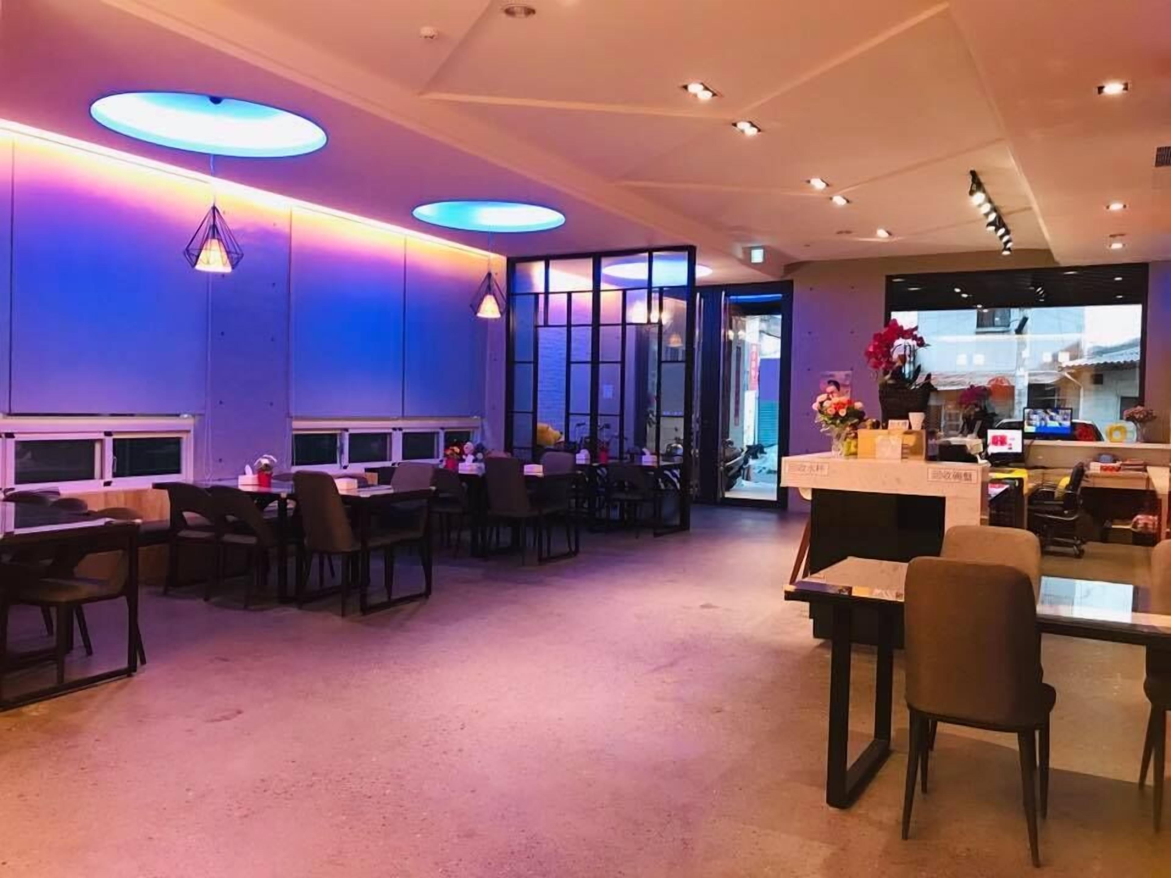 A modern hotel lobby with a reception desk, seating area, and a view of the street.