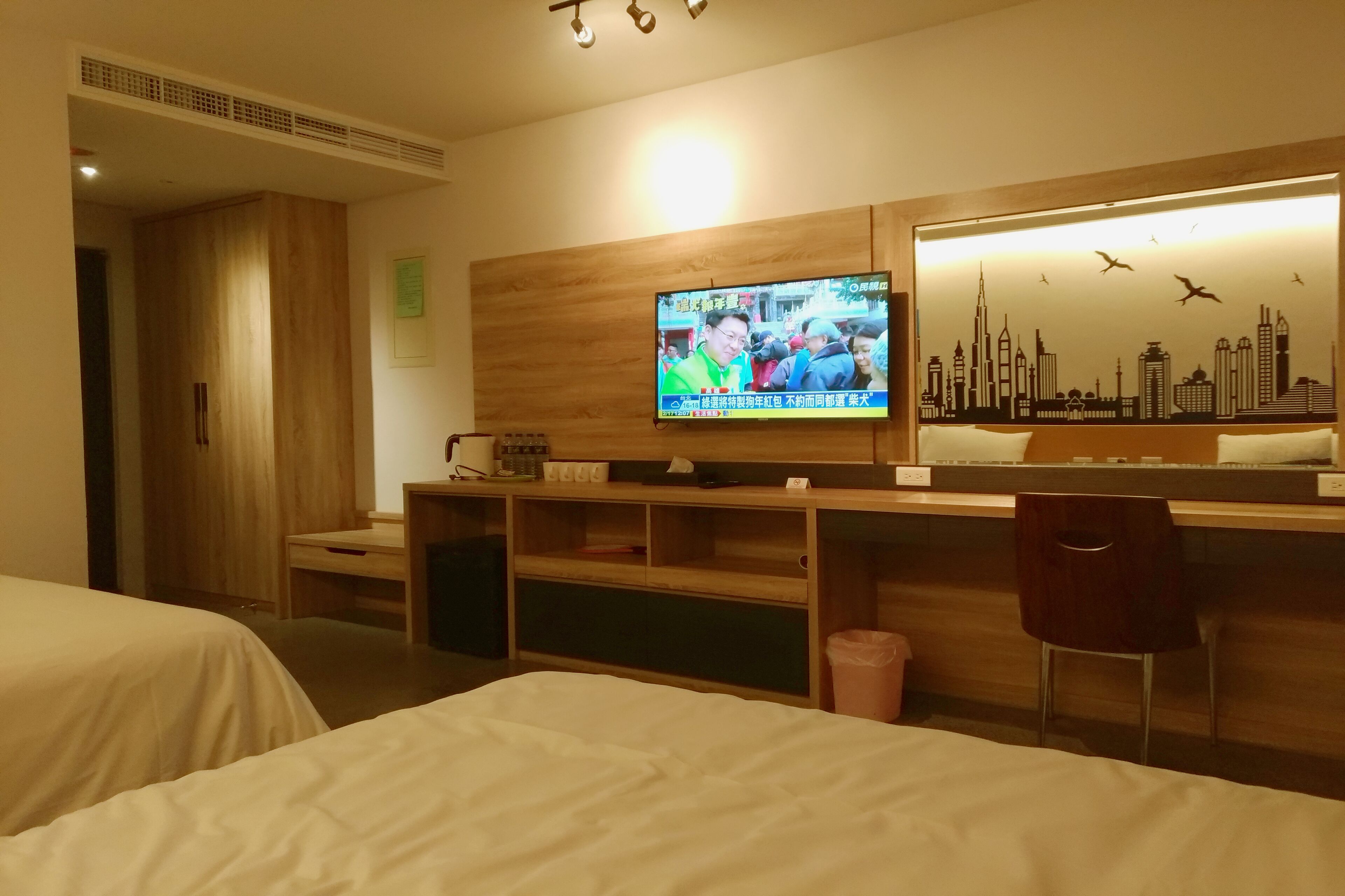 A hotel room with a bed, a desk, a TV, and a cityscape mural.