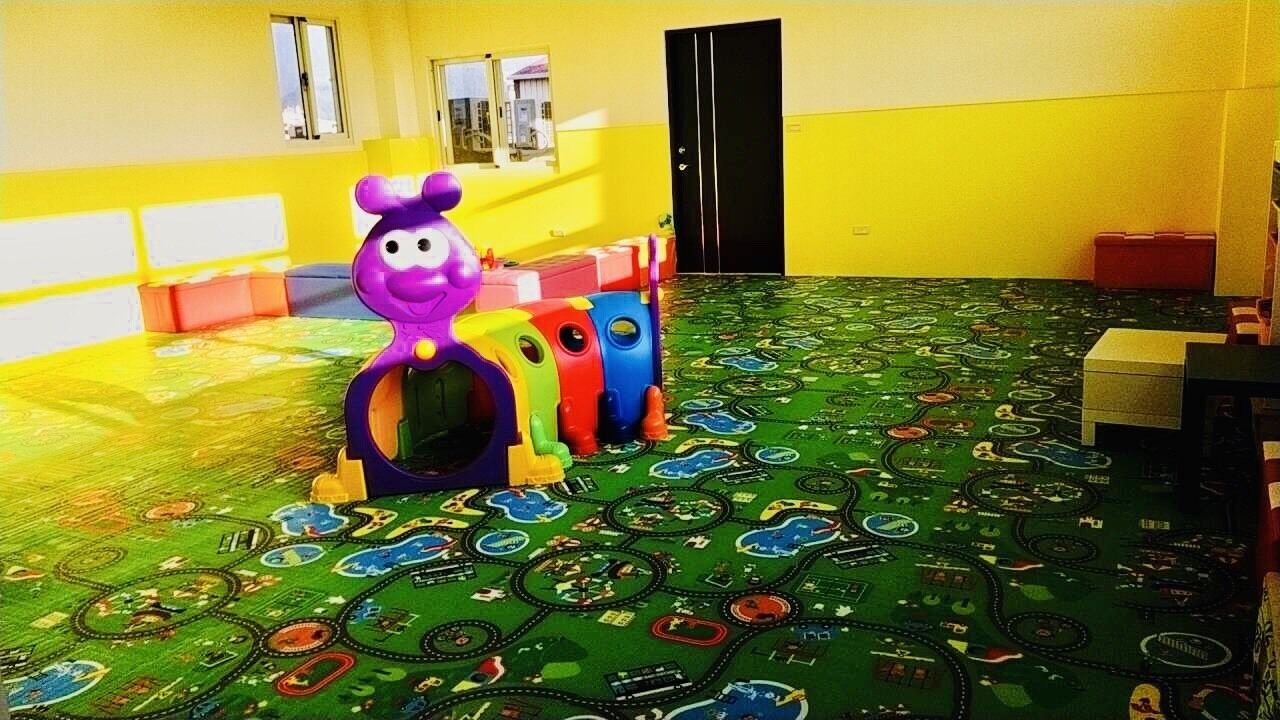 A playroom with a colorful playset and a green play mat with various designs.