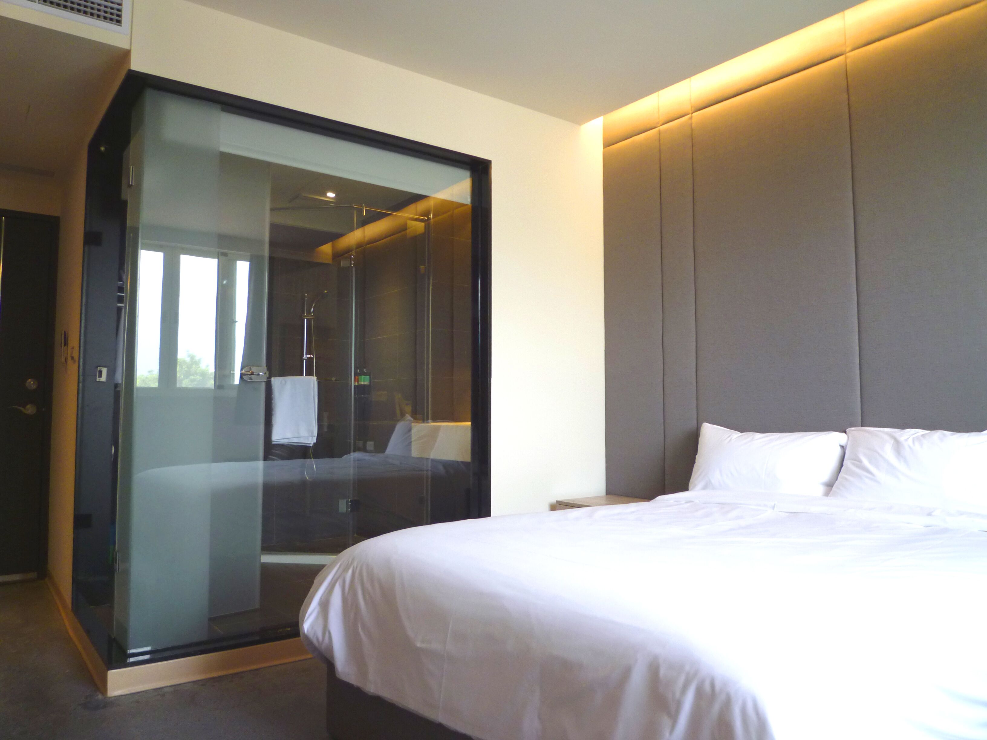 A modern hotel room with a large bed, a glass-enclosed shower area, and a large padded headboard.