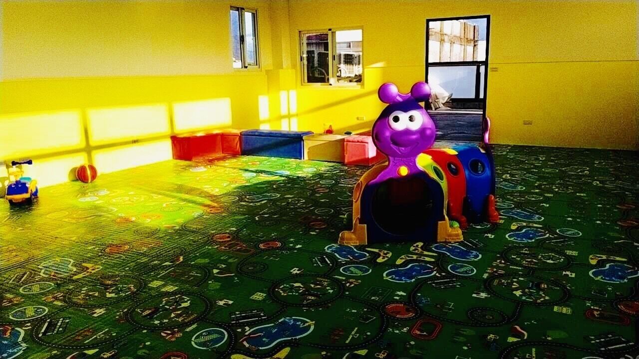 A room with a colorful play mat, a purple toy, and a window with a view of a building.