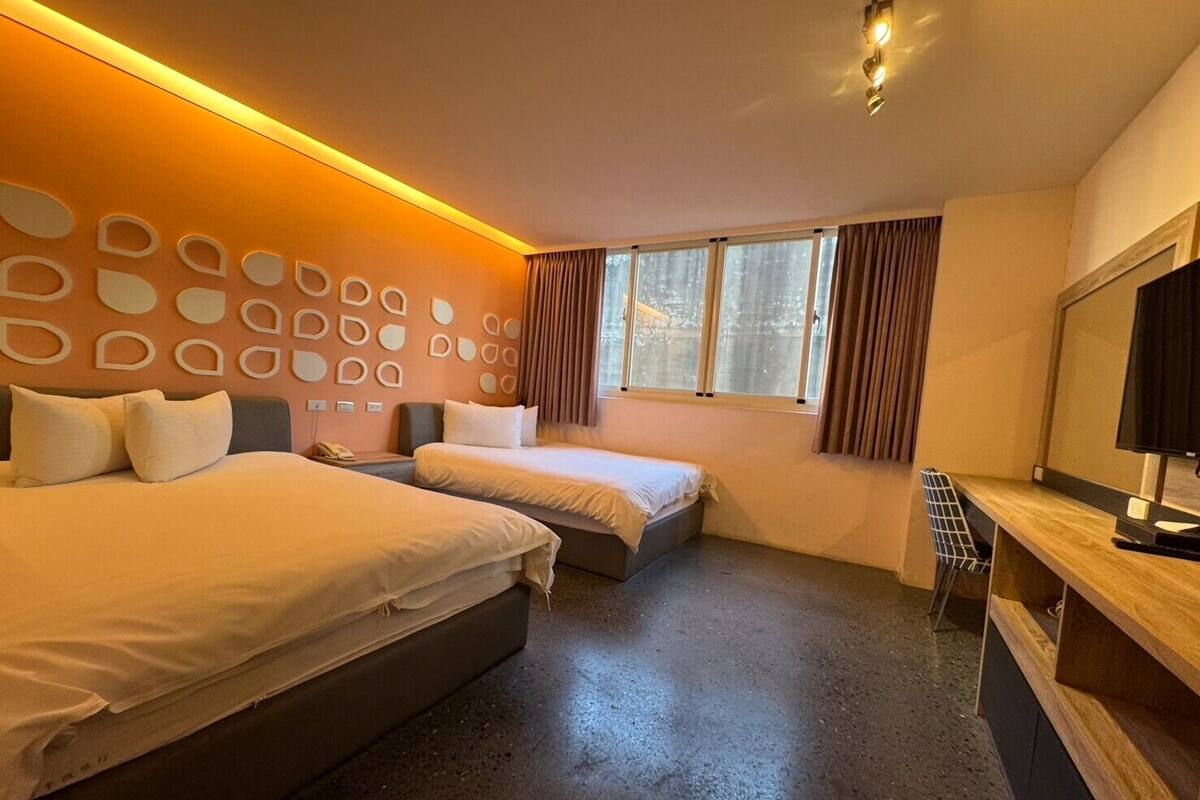 Habitación de hotel con dos camas, un escritorio, un televisor y una ventana con cortinas.