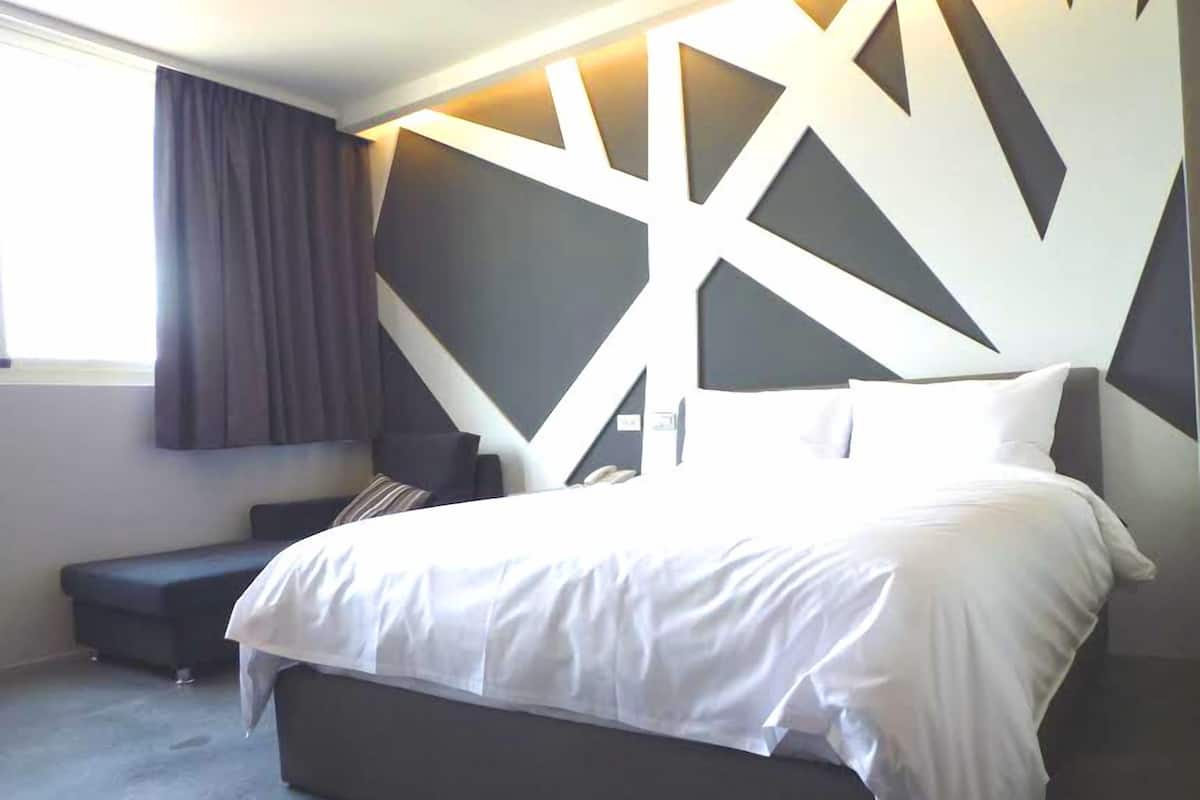 Un dormitorio moderno con una cama grande, un banco de color oscuro y un diseño geométrico en la pared.