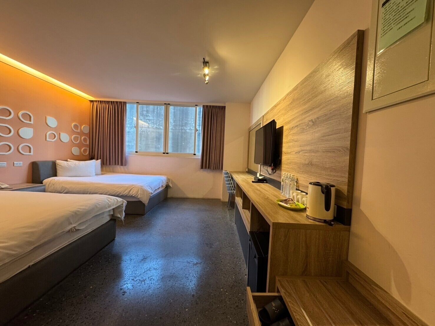 Habitación de hotel con dos camas, un escritorio con televisor y una ventana con cortinas.