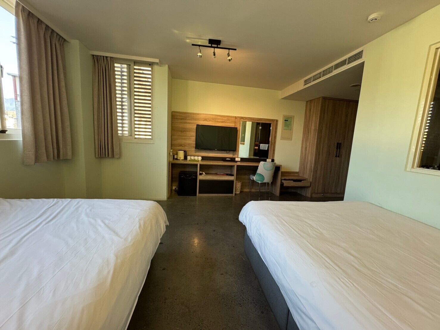 A hotel room with two beds, a desk with a computer, a TV, and a wardrobe.