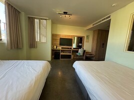 Quarto de hotel com duas camas, uma escrivaninha com computador, televisão e guarda-roupa.