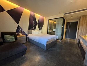A modern bedroom with a large bed, a seating area, a glass-enclosed shower, and a dark-toned wardrobe. - Travel Light Hotel (Puli)